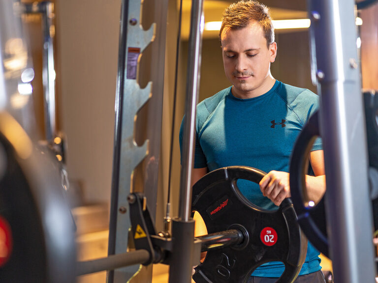 Mann trainiert mit Gewichten im Fitnessraum 4 Sterne Wellnesshotel Hüttenhof