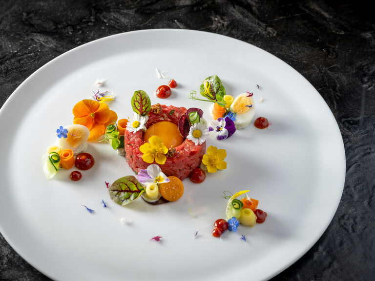Kulinarische Genüsse im Hotel Hüttenhof Beef Tatar auf weißem Teller mit Blüten, Wachteleier