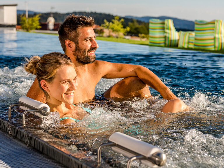 Ein Paar genießt die Blubberblasen im Whirlpool des Wellnesshotels Der Hüttenhof bei strahlender Sonne.