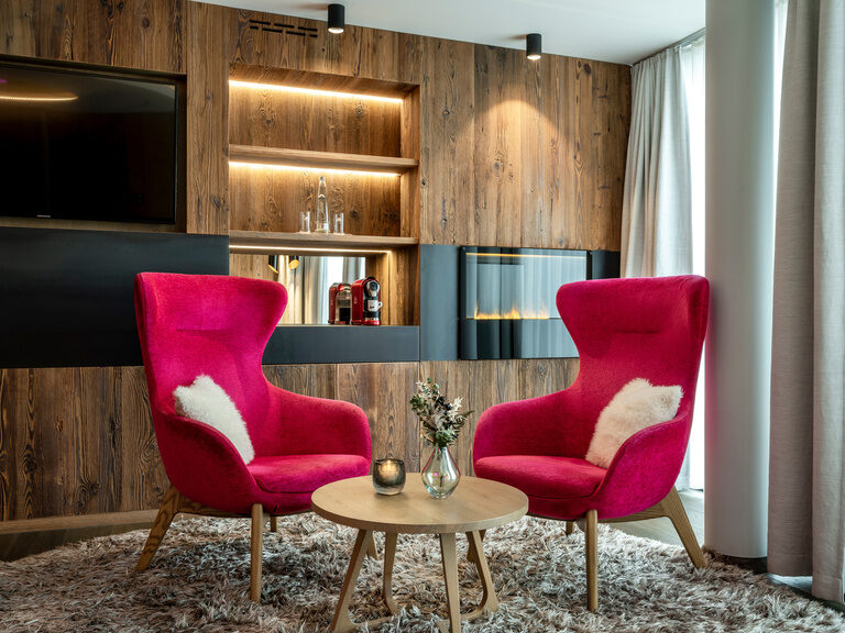 Zimmereinrichtung mit geschmackvollen, großen, pinken Stühlen vor einer großen Wohnwand aus Holz mit integriertrem Kamin